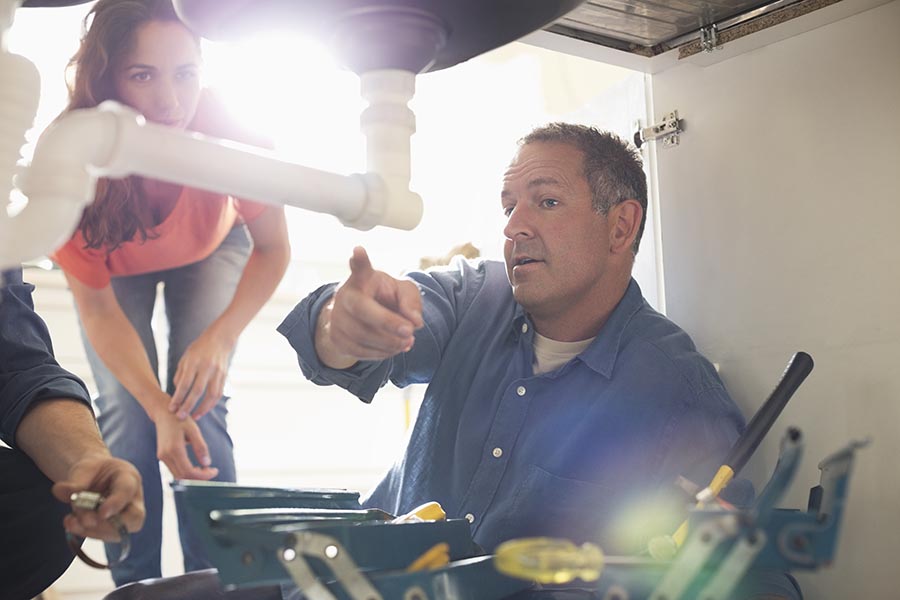 Business Insurance - Plumber Points Out Issues To a Homeowner, as He Crouches Under the Sink