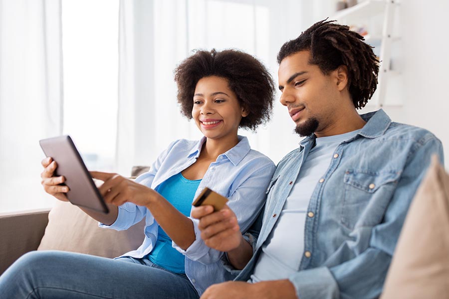 Client Center - Young Couple Use a Tablet on Their Couch, Husband Ready With a Credit Card